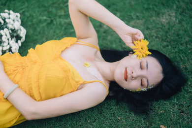 穿黄裙子手拿鲜花躺在草坪上的美丽女孩人像