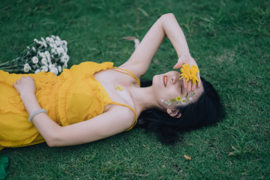 穿黄裙子手捧鲜花躺在草坪上的美丽女孩人像