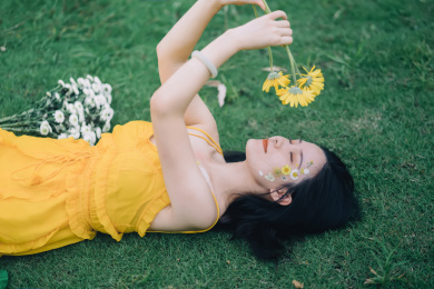 穿黄裙子手捧鲜花躺在草坪上的美丽女孩人像