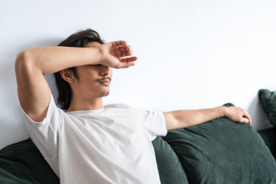 一名年轻男性坐在沙发上用手挡着眼睛	