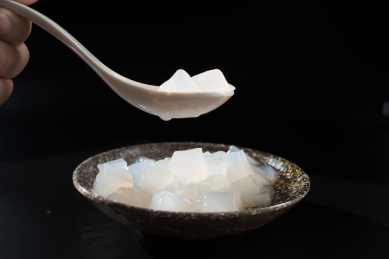 黑背景中一只手拿着白色汤勺盛装着瓷碗的椰子肉