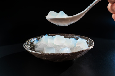 黑背景中一只手拿着白色汤勺盛装着瓷碗的椰子肉