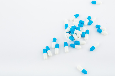 白色背景纸上放着蓝白色胶囊和白色药瓶。