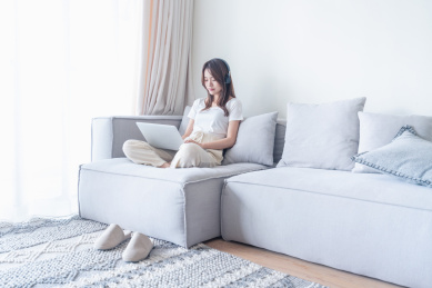 一名年轻的亚洲女子坐在客厅的沙发上使用电脑