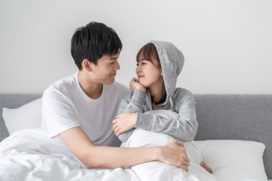 坐在床上相互对视微笑的年轻情侣