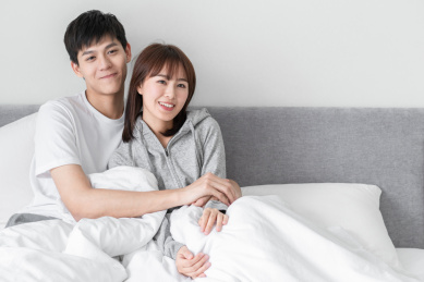 坐在床上相互倚靠微笑的年轻情侣