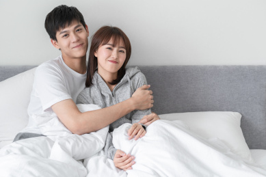 坐在床上相互倚靠微笑的年轻情侣