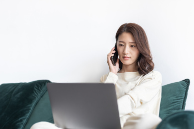年轻漂亮的女性坐在沙发一边使用电脑一边打电话