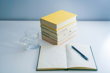 一摞书一个打开的笔记本和一杯水放在白色桌面上