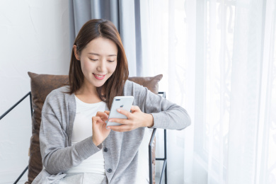 一名年轻女性坐在客厅窗边的沙发椅上玩手机