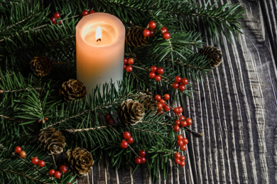 摆放在木质桌面上的圣诞树、红浆果和燃烧中的白色蜡烛