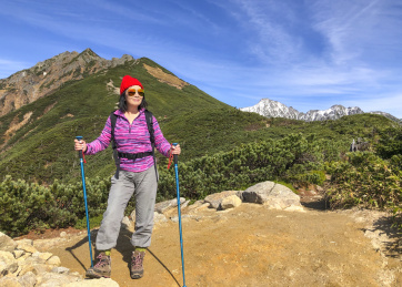 一个手拿登山杖站在山顶看着远方的女性徒步旅行者