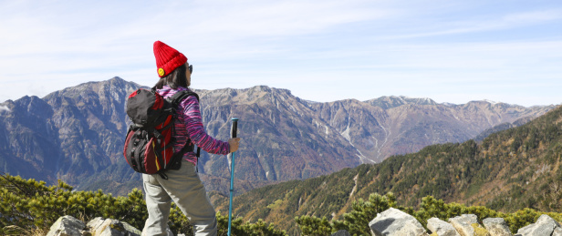 一个手拿登山杖站在山顶看着远方的女性徒步旅行者背影