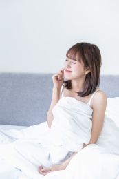 年轻女性坐在床上闭眼笑着摸自己的脸