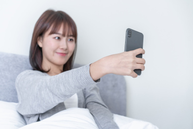 年轻女性半坐在床上用手机自拍