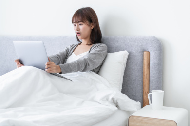 年轻女性坐在床上吃惊地看着电脑