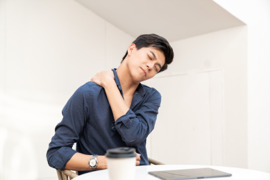 一名年轻的商务男士坐在室外的椅子上按摩颈部