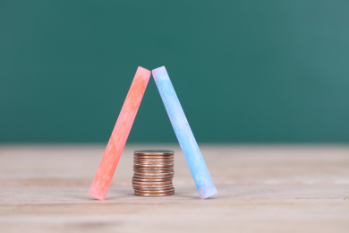 两只教学用的彩色粉笔在桌子上摆成人字的形状及下面一摞美元硬币