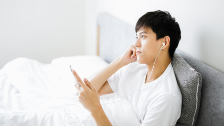 卧室里的男孩在床上使用手机听音乐