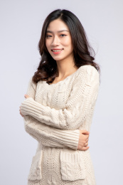 灰色背景里，身穿米色毛衣的美丽亚洲女孩