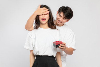 灰色背景里，手里拿着礼物盒的亚洲年轻情侣