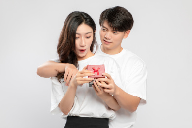 灰色背景里，手里拿着礼物盒的亚洲年轻情侣