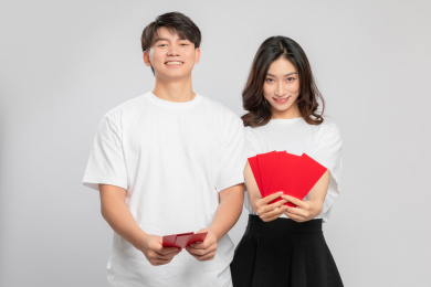  灰色背景里，手里拿着红包正在拜年的亚洲年轻情侣