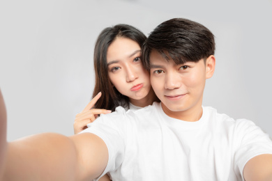 灰色背景里，正在自拍的亚洲年轻情侣