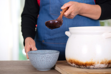 厨房里戴着围裙的人把熬好的腊八粥盛到碗里