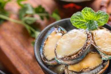 放在木板上的装有新鲜食材鲍鱼的黑色碗