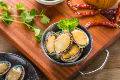 放在木板上的装有新鲜食材鲍鱼的黑色碗