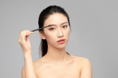  灰色背景里正在使用眉笔的亚洲美女面部特写，化妆护肤整容