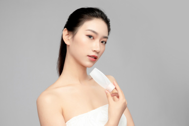  灰色背景里手中拿着洗面奶瓶子作为展示的亚洲美女面部特写，化妆护肤整容