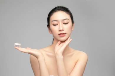 灰色背景里手中拿着塑料小瓶作为展示的亚洲美女面部特写，化妆护肤整容