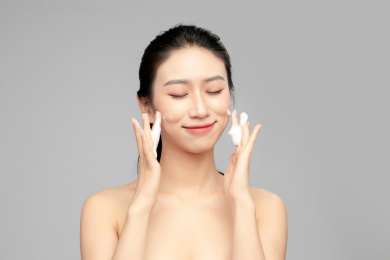 灰色背景里正在使用洗面奶的亚洲美女面部特写，化妆护肤整容