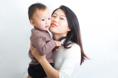 年轻的妈妈抱着亲吻可爱的小孩子