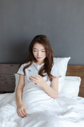 卧室里一名年轻女性坐在床上玩手机