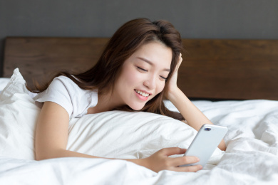 卧室里一名年轻女性趴在床上玩手机