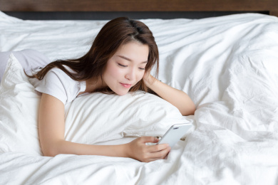卧室里一名年轻女性趴在床上玩手机