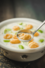 暗色木纹桌面上放着一份菌菇丝瓜煮鱼腐