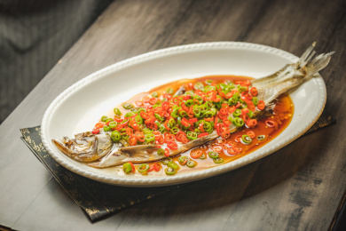  暗色木纹桌面上放着一份清蒸太湖白鱼