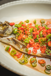  暗色木纹桌面上放着一份清蒸太湖白鱼