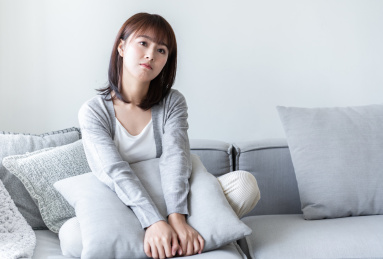 年轻女性盘腿坐在沙发上抱着抱枕在发呆