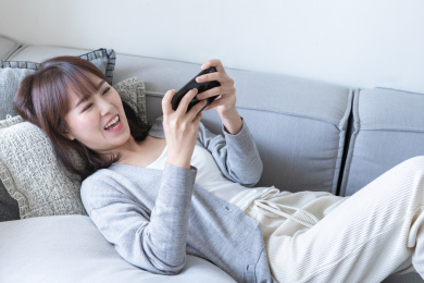 年轻女性躺在沙发靠垫上用手机玩游戏