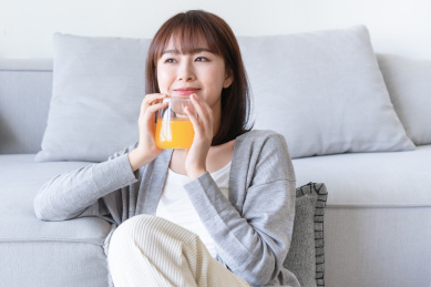 年轻女性双手捧着橙汁靠在沙发边上
