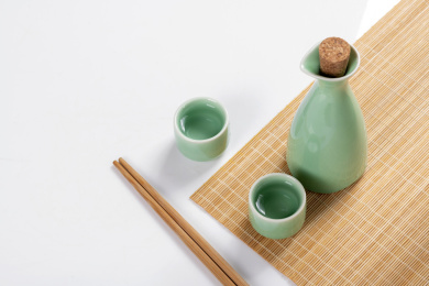 梅子青酒壶酒杯摆放在红色洒金背景上旁边放有中国结木托盘