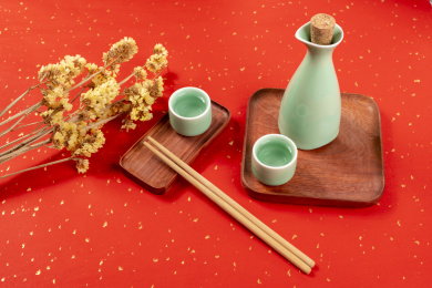 梅子青酒壶酒杯摆放在红色洒金背景上旁边放有中国结木托盘