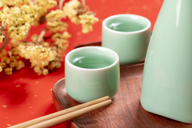 梅子青酒壶酒杯摆放在红色洒金背景上旁边放有中国结木托盘