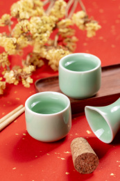 梅子青酒壶酒杯摆放在红色洒金背景上旁边放有中国结木托盘
