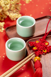 梅子青酒壶酒杯摆放在红色洒金背景上旁边放有中国结木托盘